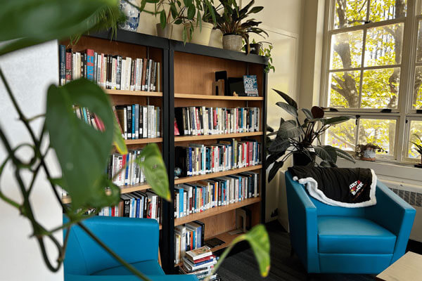 Cozy reading area with bookshelves, blue armchairs, and potted plants by large windows.